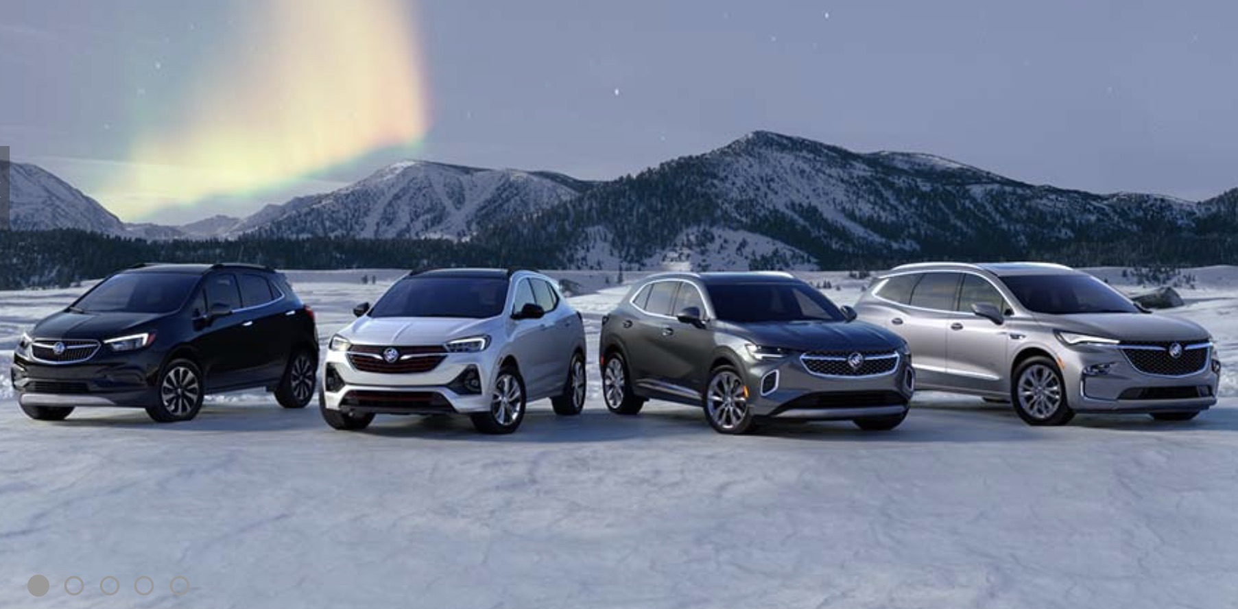 4 Buick vehicles parked in front of a mountain range on a bed of snow, with the Northern Lights in the background.