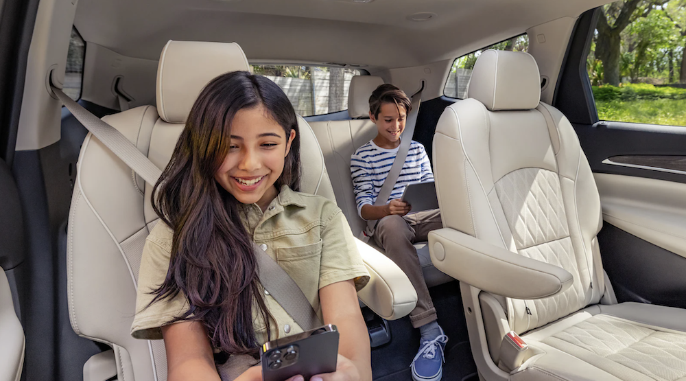 A young boy and a girl buckled into the back seat of an SUV both playing on electronics.